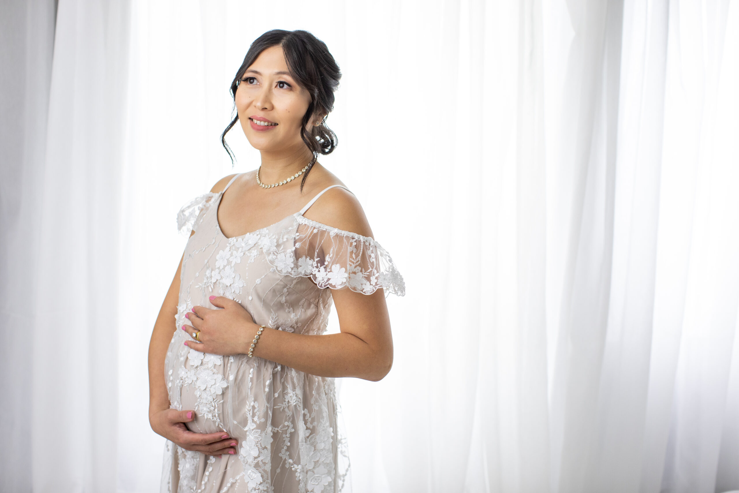 Studio maternity portrait in Pink Blush lace gown on back lit white background.