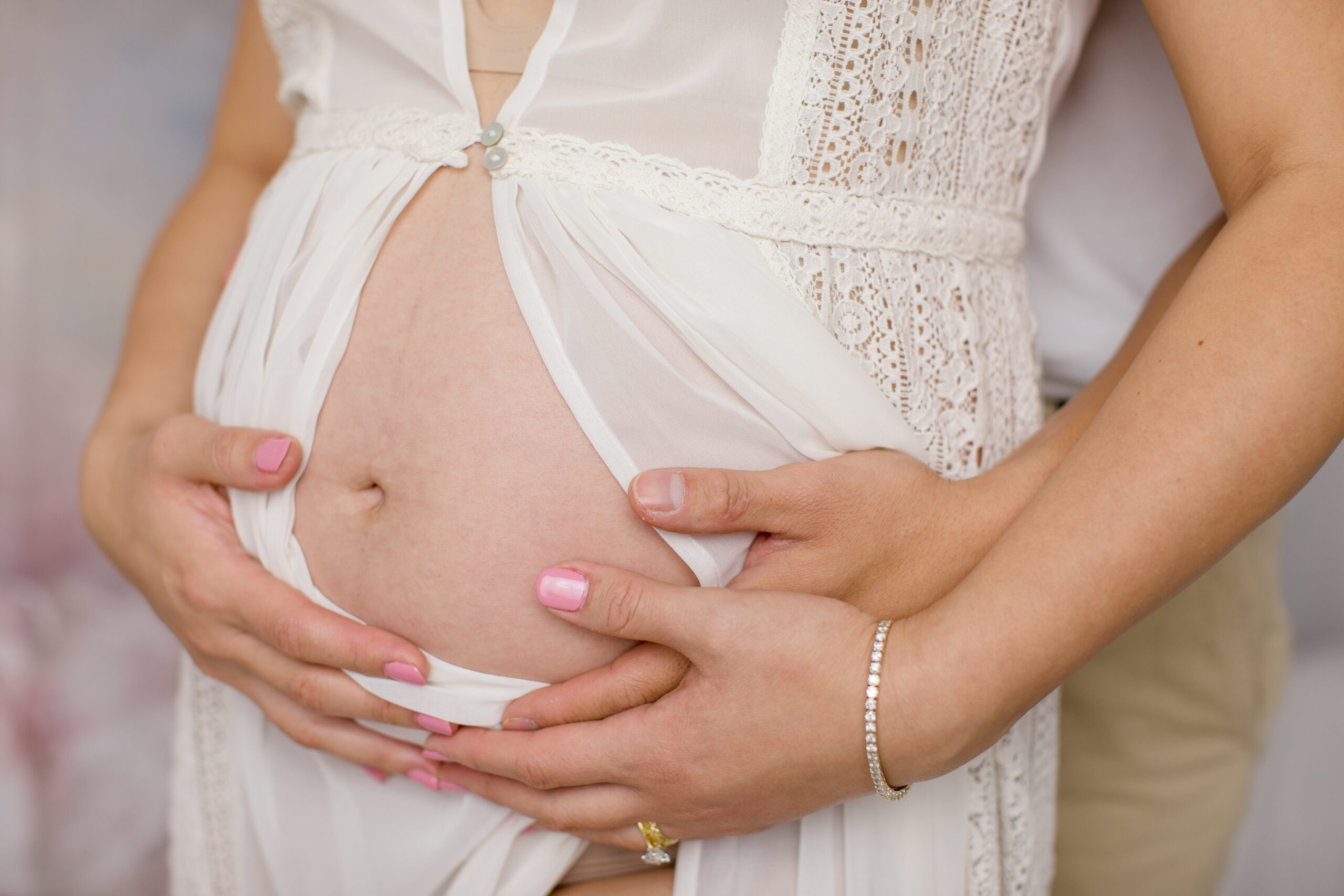 Close up of pregnant belly with soft light colors and lace texture.